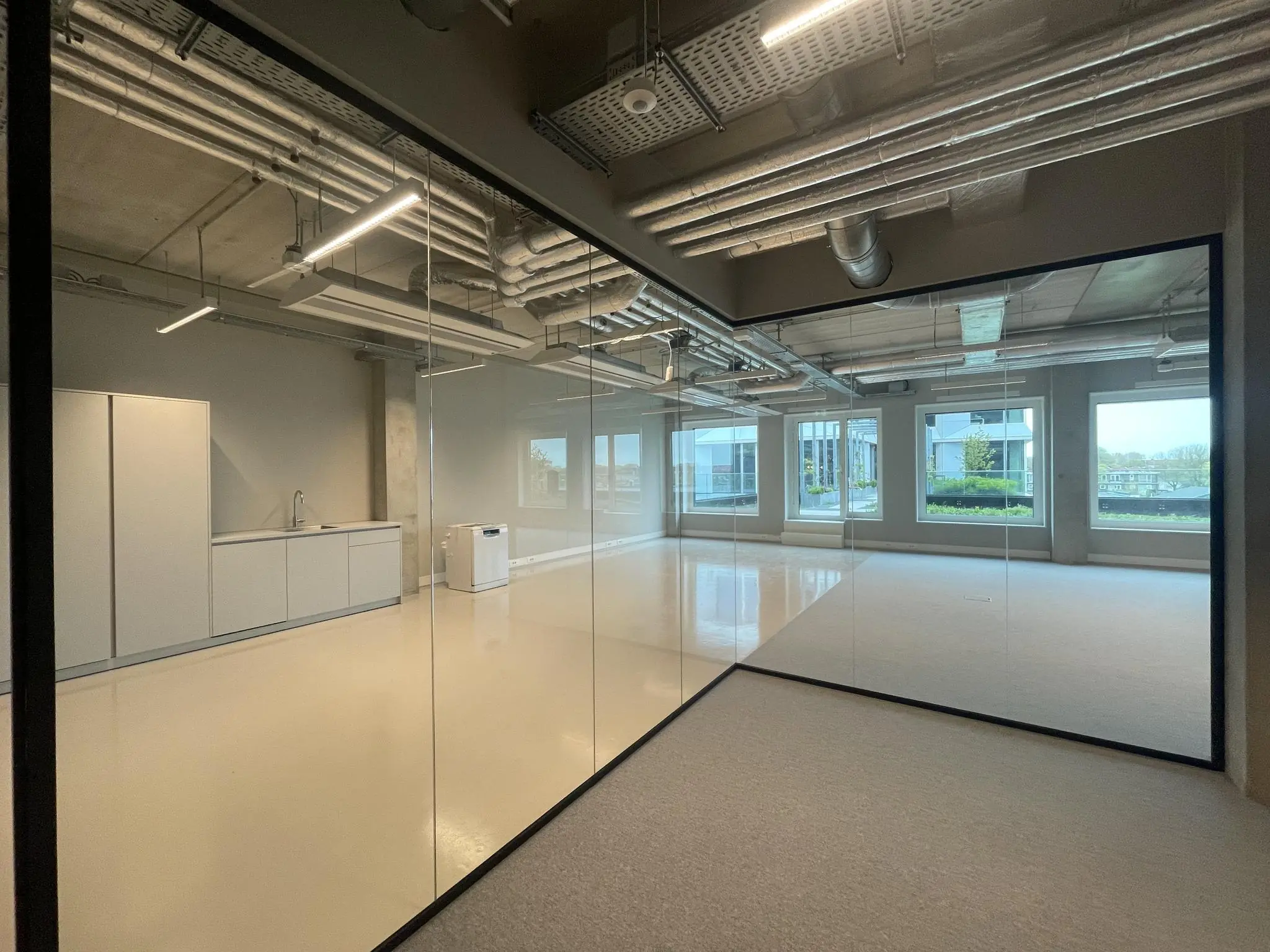 Moderne, lege kantoorruimte aan de Asterweg met glazen wanden, keukenblok en zicht op buiten.