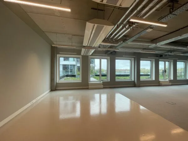 Lichte, lege kantoorruimte aan de Asterweg met grote ramen en zicht op een binnentuin en stad.