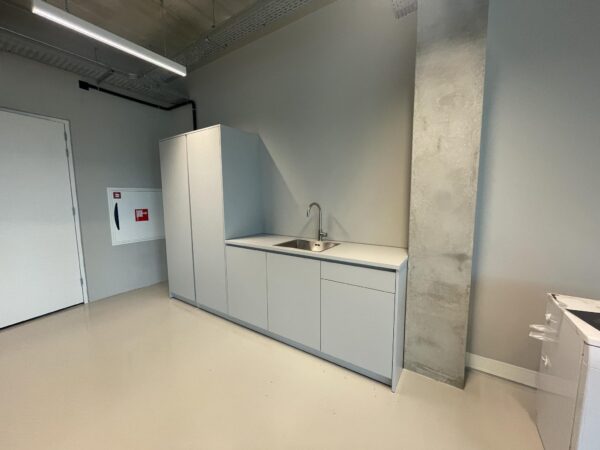 Minimalistische grijze pantry met inbouwspoelbak en hoge kast in een strak afgewerkte ruimte aan de Asterweg.