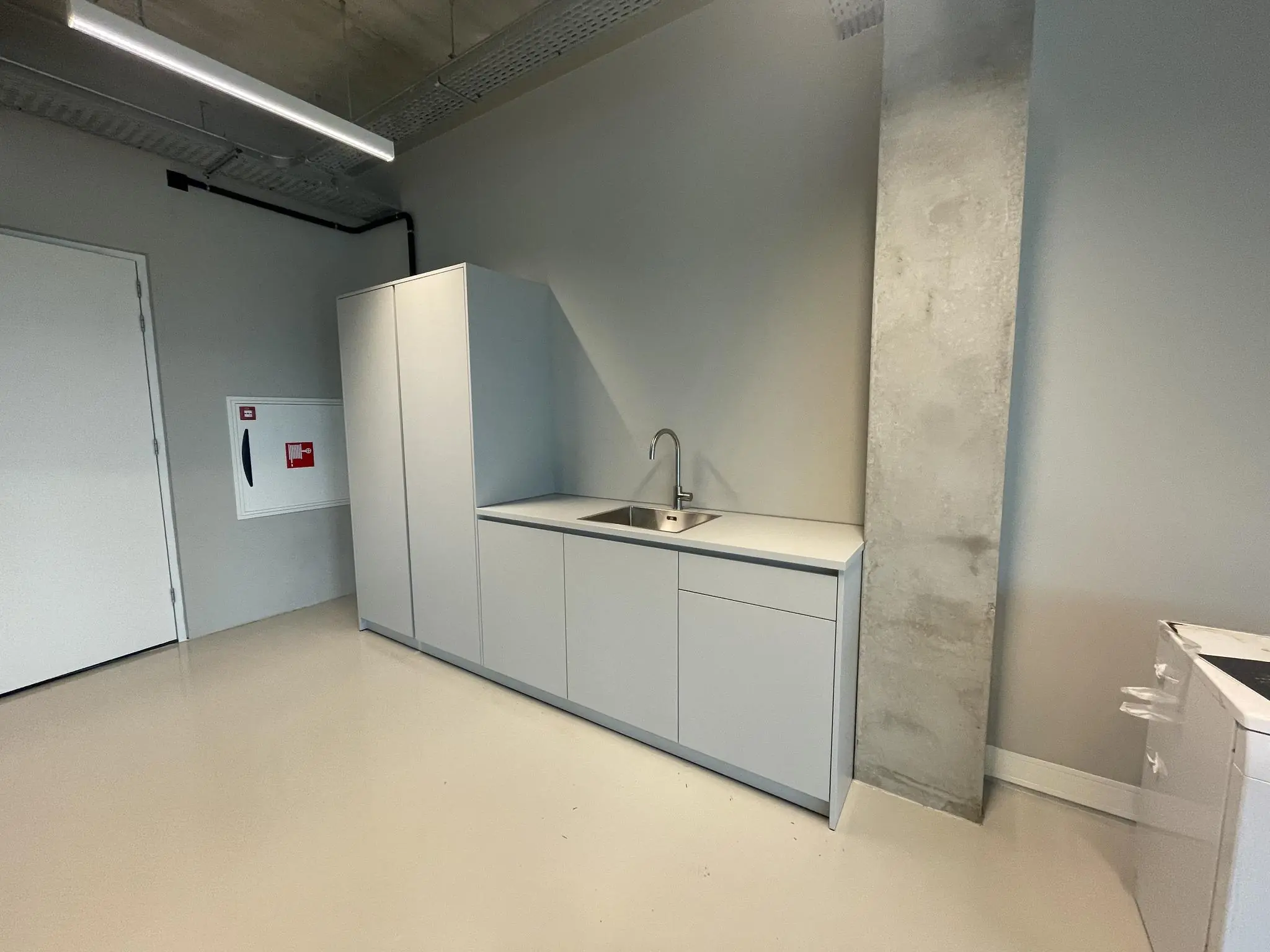 Minimalistische grijze pantry met inbouwspoelbak en hoge kast in een strak afgewerkte ruimte aan de Asterweg.