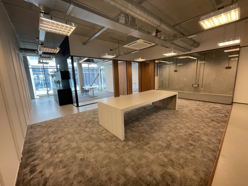 Moderne kantoorruimte aan de Danzigerkade met glazen wanden, industriële plafonds en een grote witte vergadertafel.