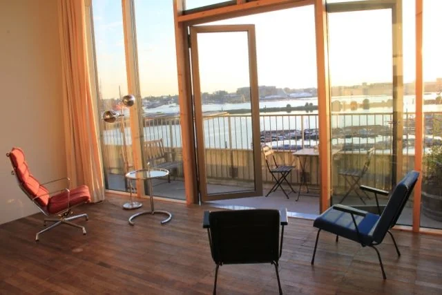 Licht ingerichte woonkamer met moderne stoelen en uitzicht op het water vanaf de Danzigerkade in Amsterdam.