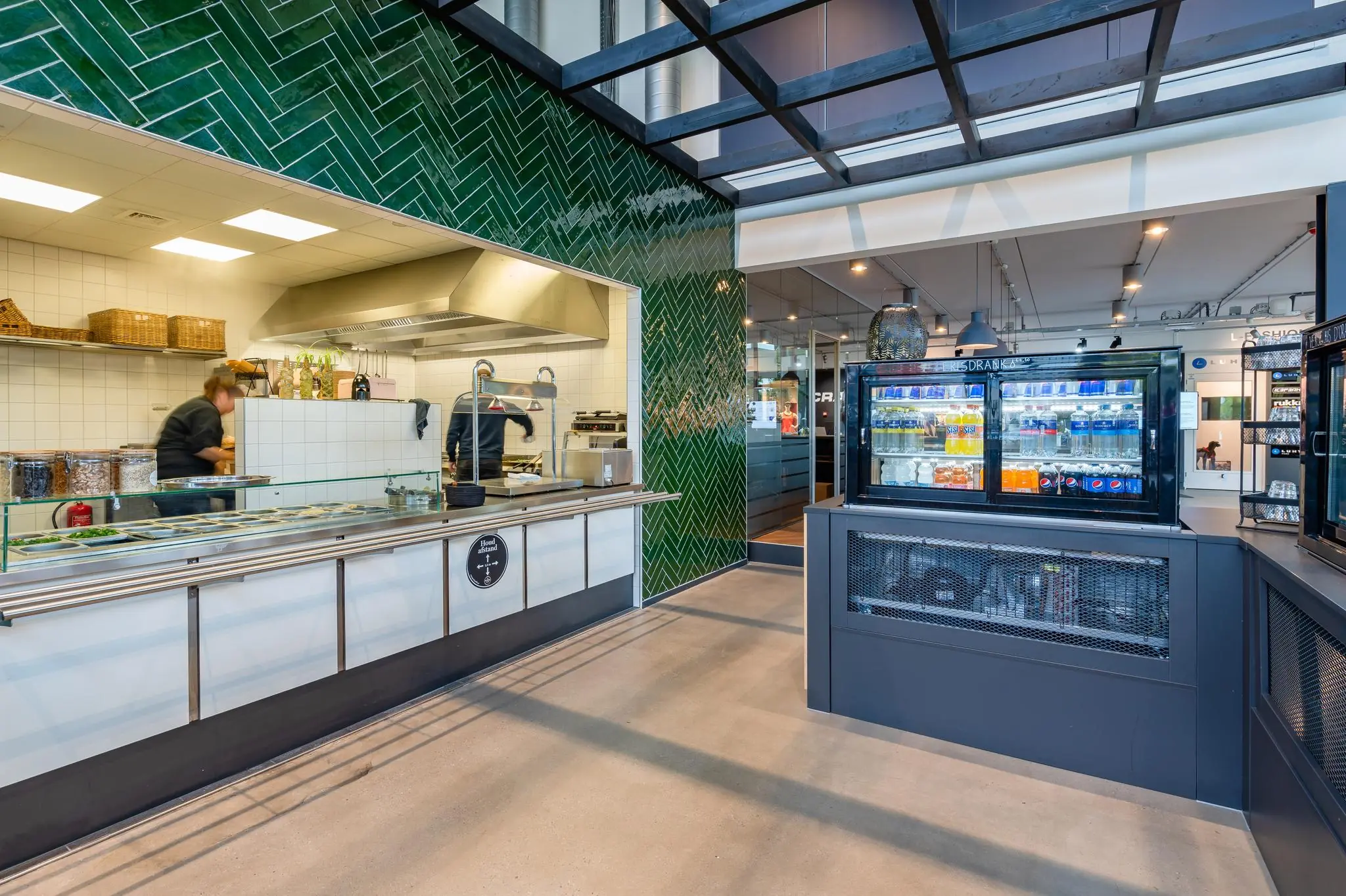 Moderne bedrijfskeuken aan de Plesmanstraat met open uitgiftebalie en een gekoelde drankdisplay.