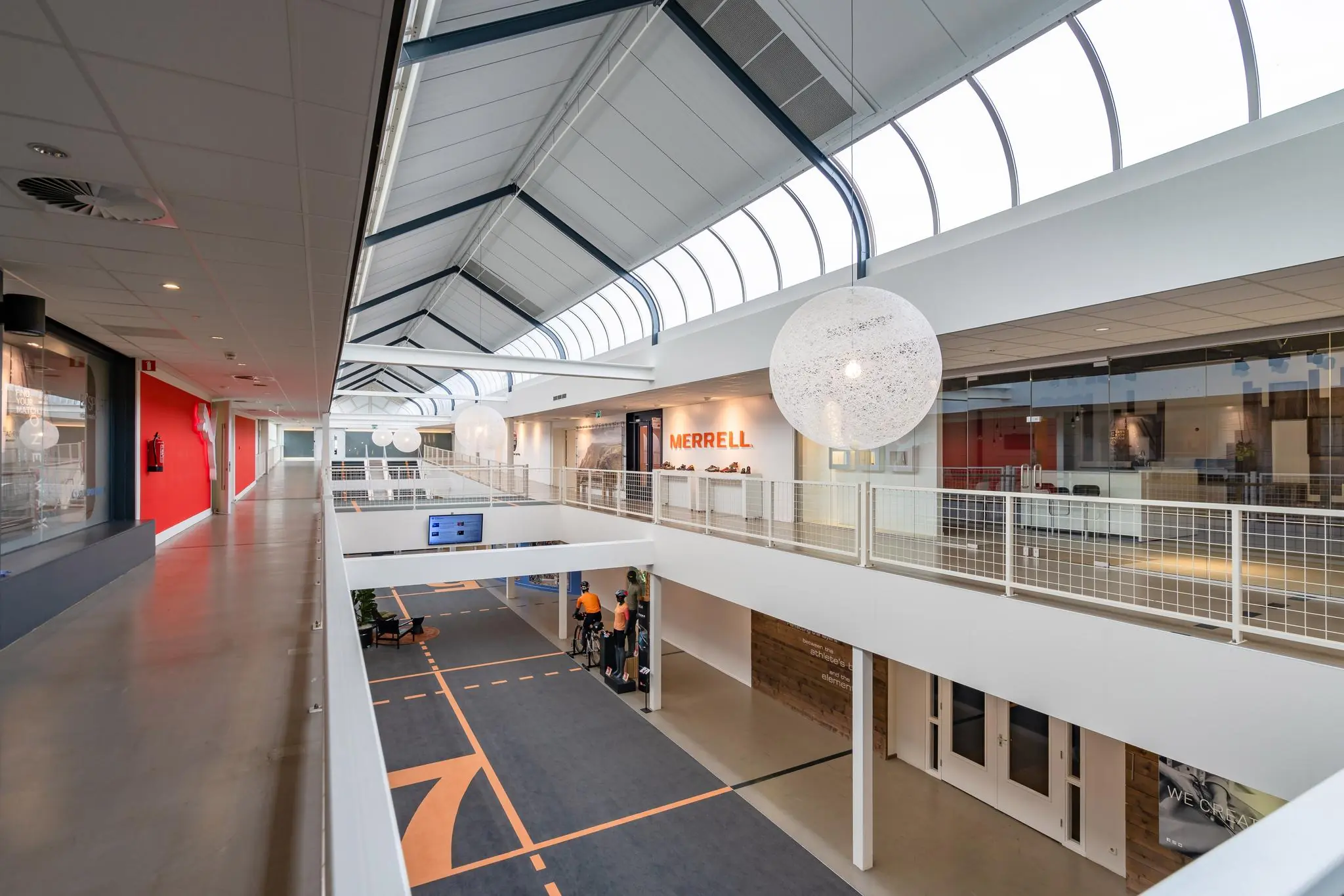 Moderne, lichtovergoten gang in een bedrijfsverzamelgebouw aan de Plesmanstraat met zicht op de winkel van Merrell.