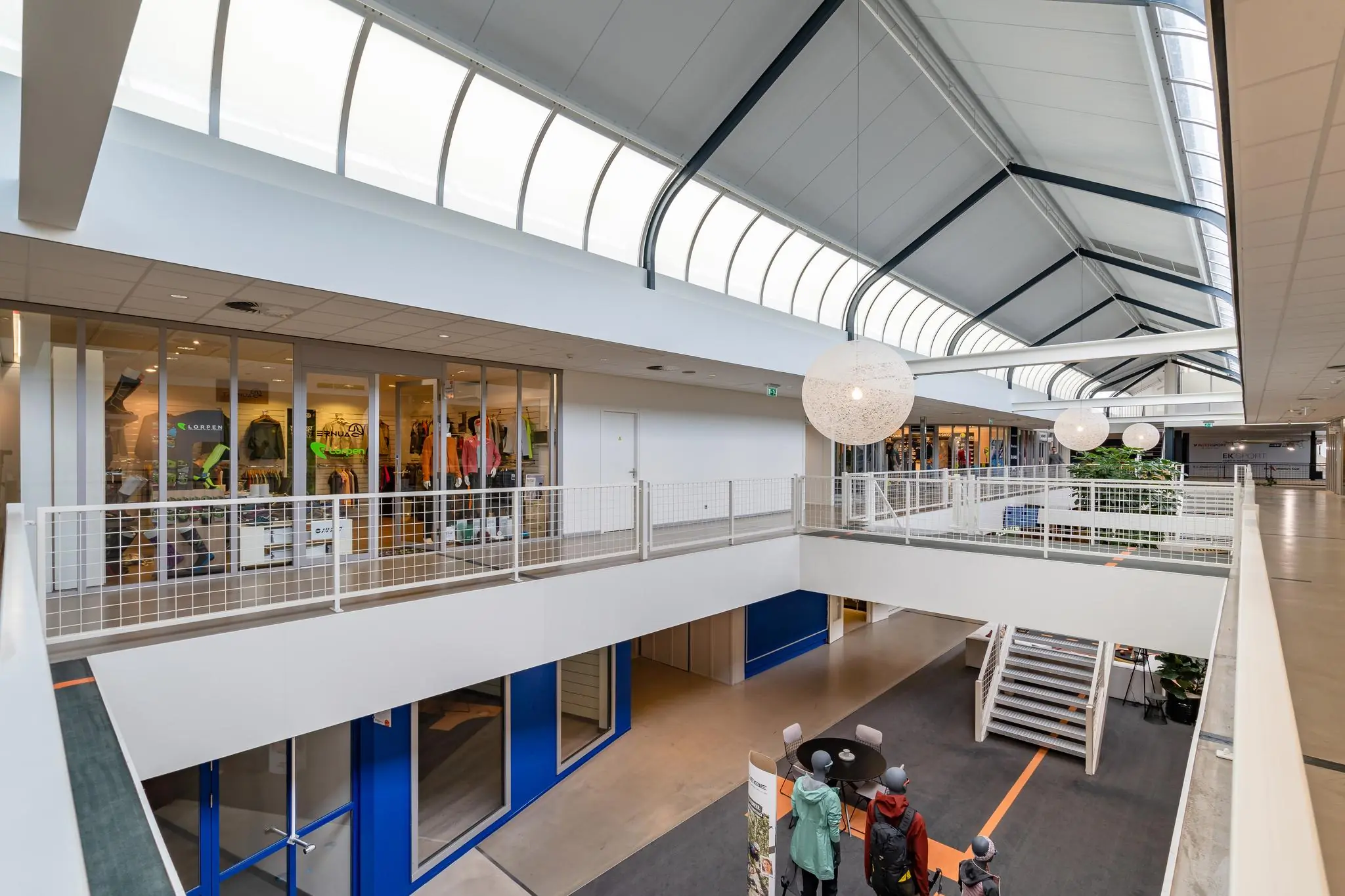 Binnenruimte van een modern bedrijfsverzamelgebouw aan de Plesmanstraat met winkels, kantoorruimtes en een trap naar de benedenverdieping.