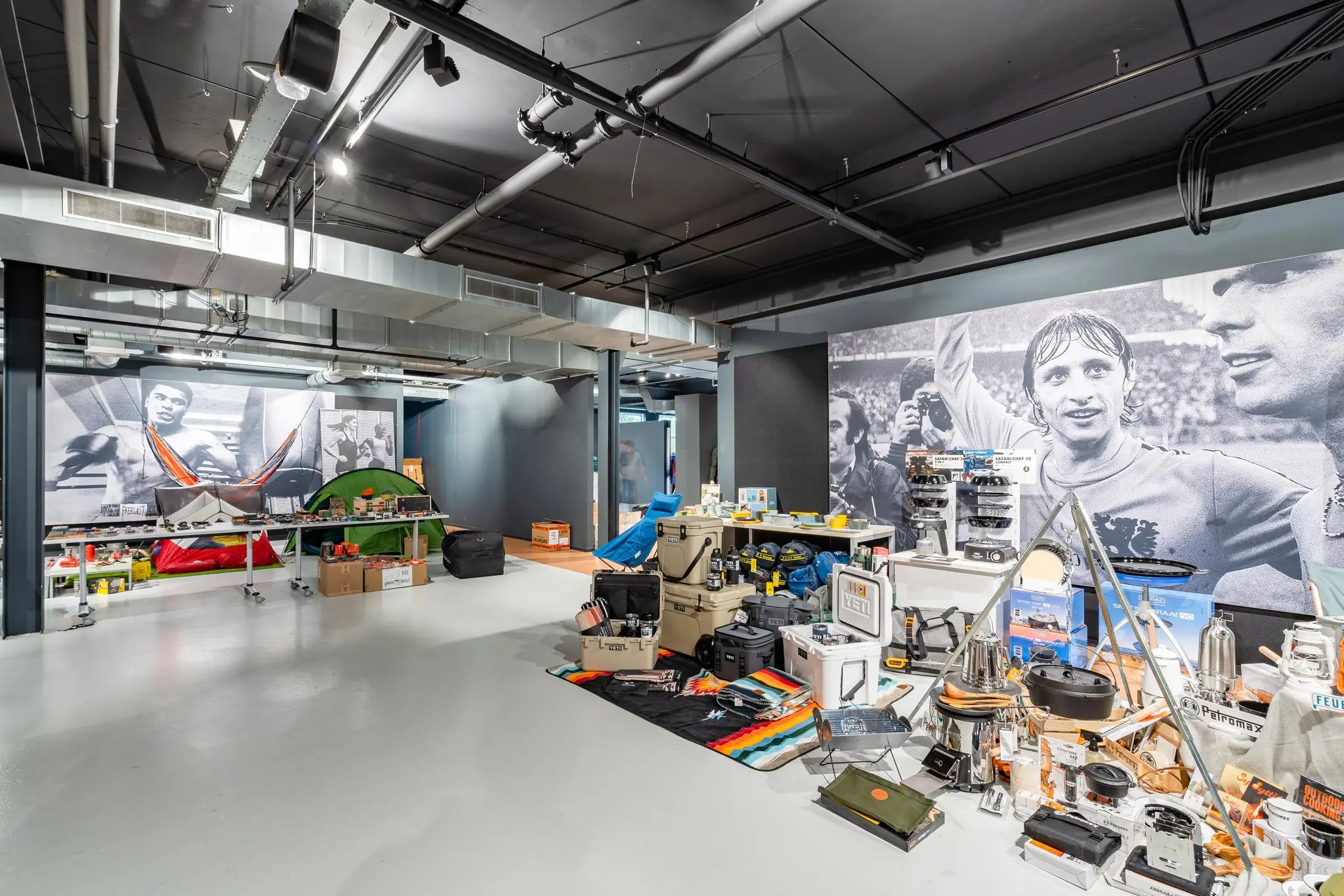 Winkelinterieur met kampeer- en outdoorartikelen, met op de achtergrond grote zwart-witfoto’s van sporticonen aan de Plesmanstraat.