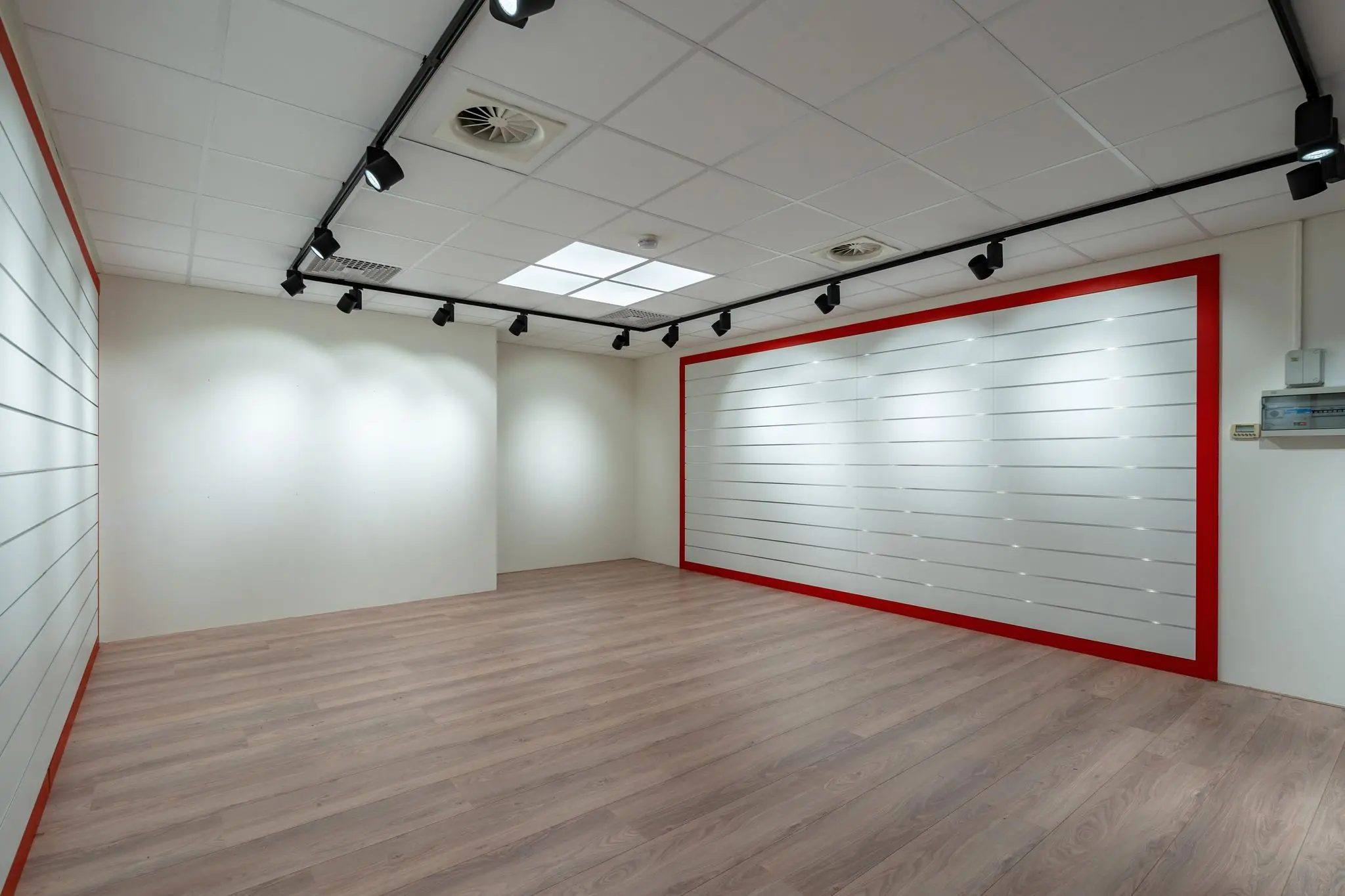 Leeg commercieel interieur aan de Plesmanstraat met laminaatvloer, systeemplafond en witte displaywanden met rode randen.