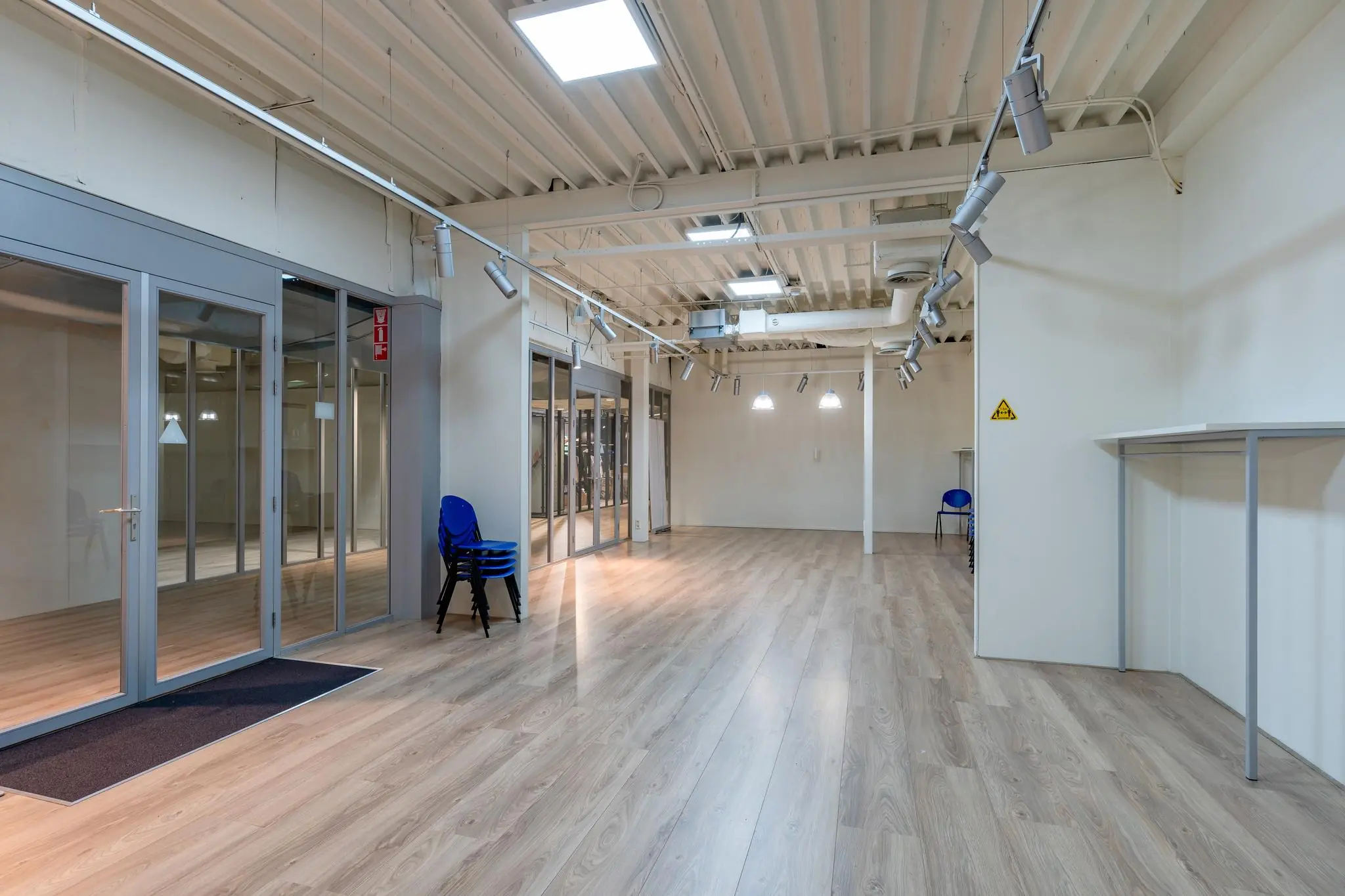 Leeg kantoorpand aan de Plesmanstraat met houten vloer, glazen wanden en enkele stapelstoelen.