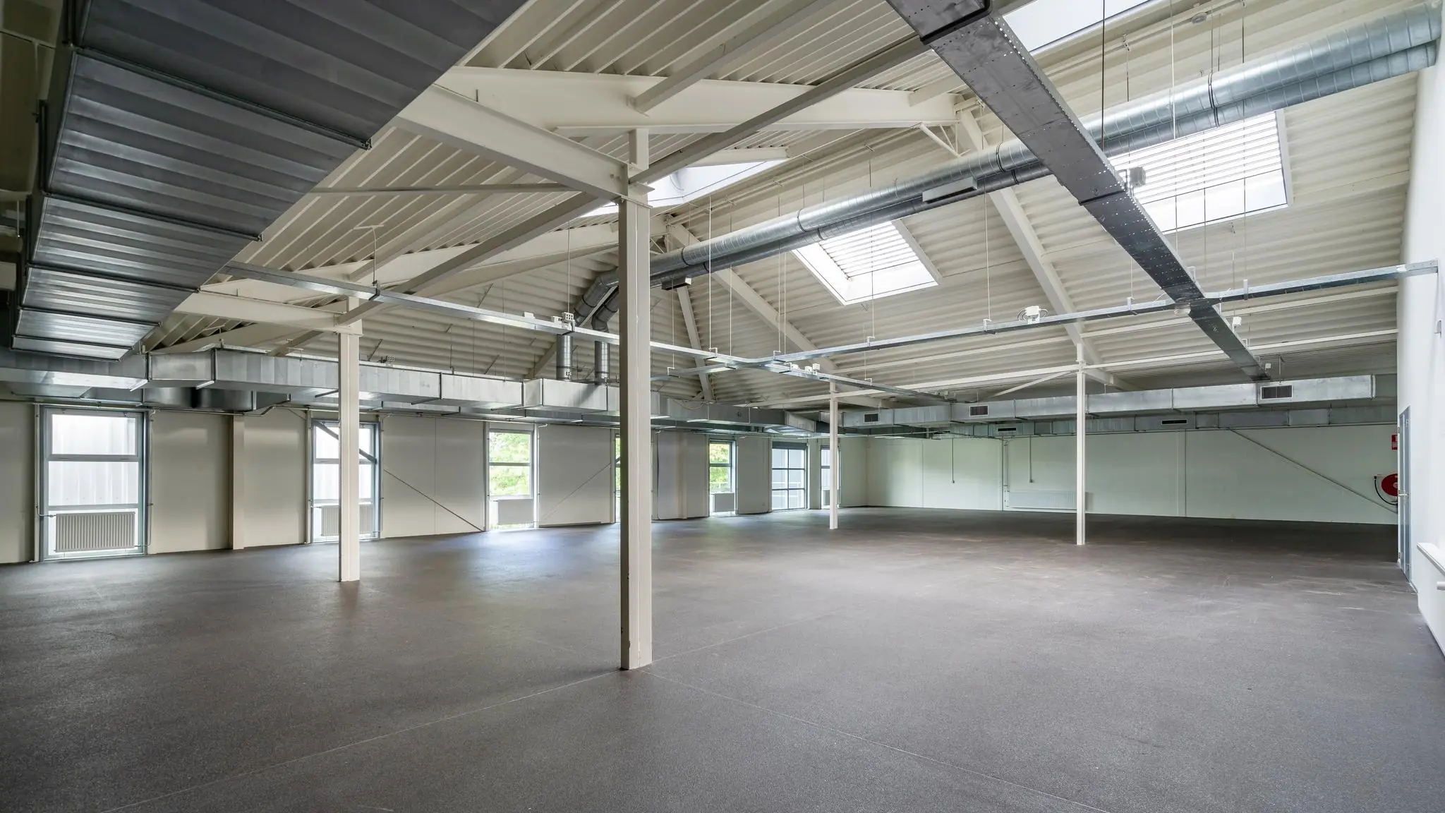 Leeg industrieel bedrijfspand aan de Plesmanstraat met hoge plafonds, grote ramen en zichtbare ventilatiebuizen.