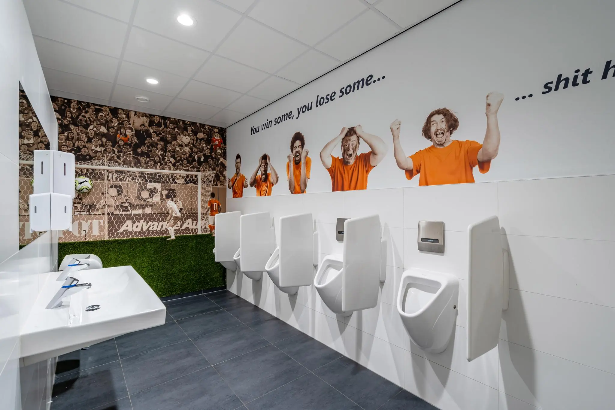 Een creatief vormgegeven herentoilet in voetbalthema met muurschilderingen van juichende fans en een doelnet achter de urinoirs.