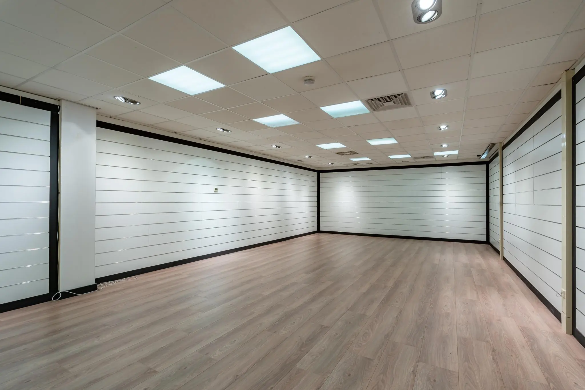 Leegstaand winkelpand aan de Plesmanstraat met witte wandpanelen, systeemplafond en houten vloer.