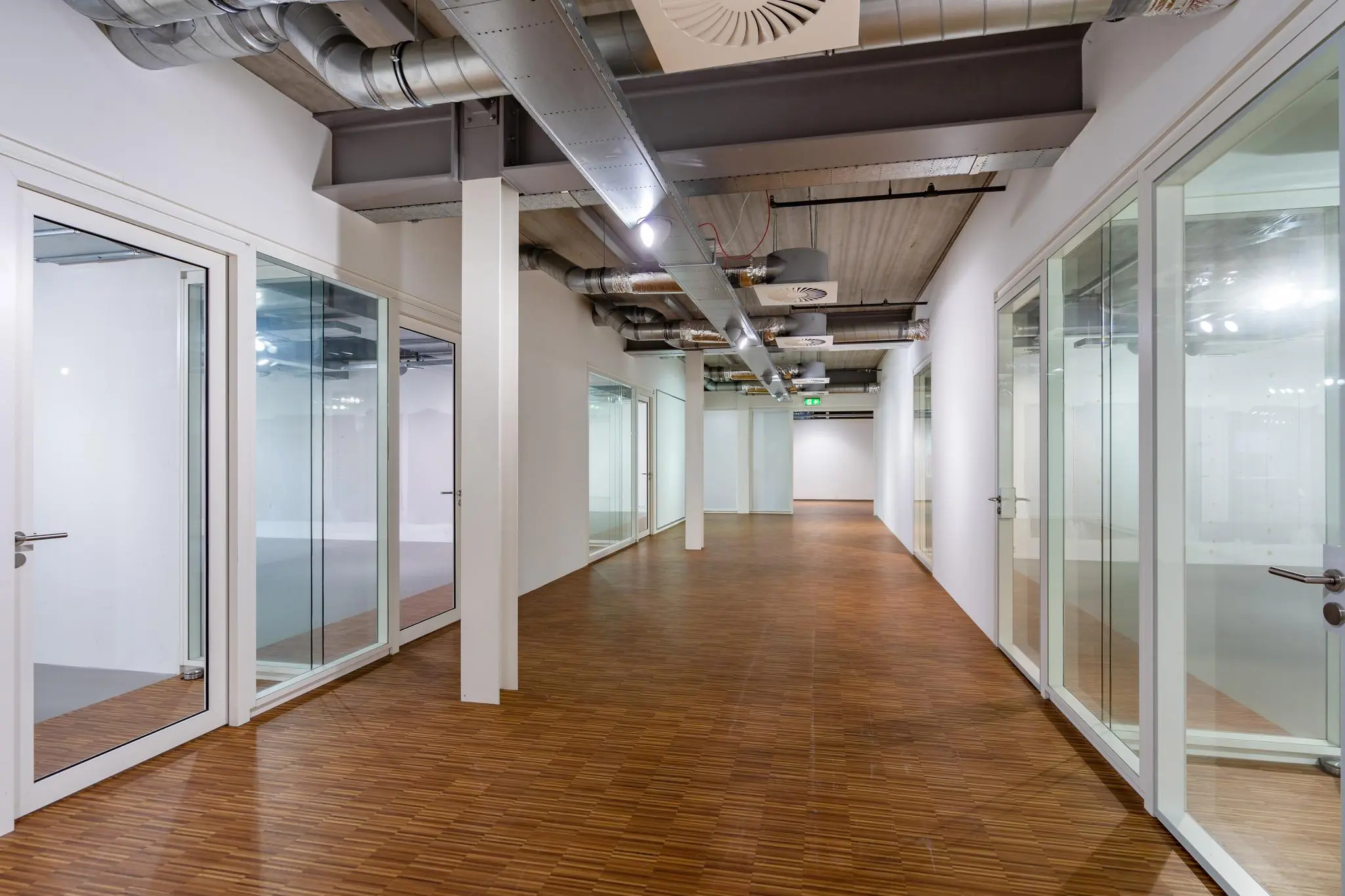 Moderne kantoorruimte aan de Plesmanstraat met glazen wanden, houten vloer en zichtbare ventilatiekanalen.