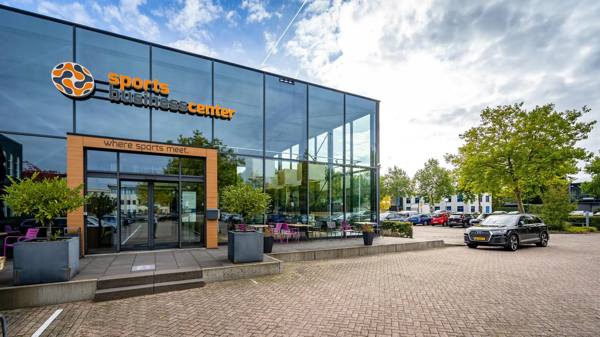 Glazen gevel van het Sports Business Center aan de Plesmanstraat met zicht op de entree en parkeerplaats.