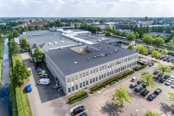 Luchtfoto van een groot kantoorpand aan de Plesmanstraat met parkeerplaatsen en omliggend groen.