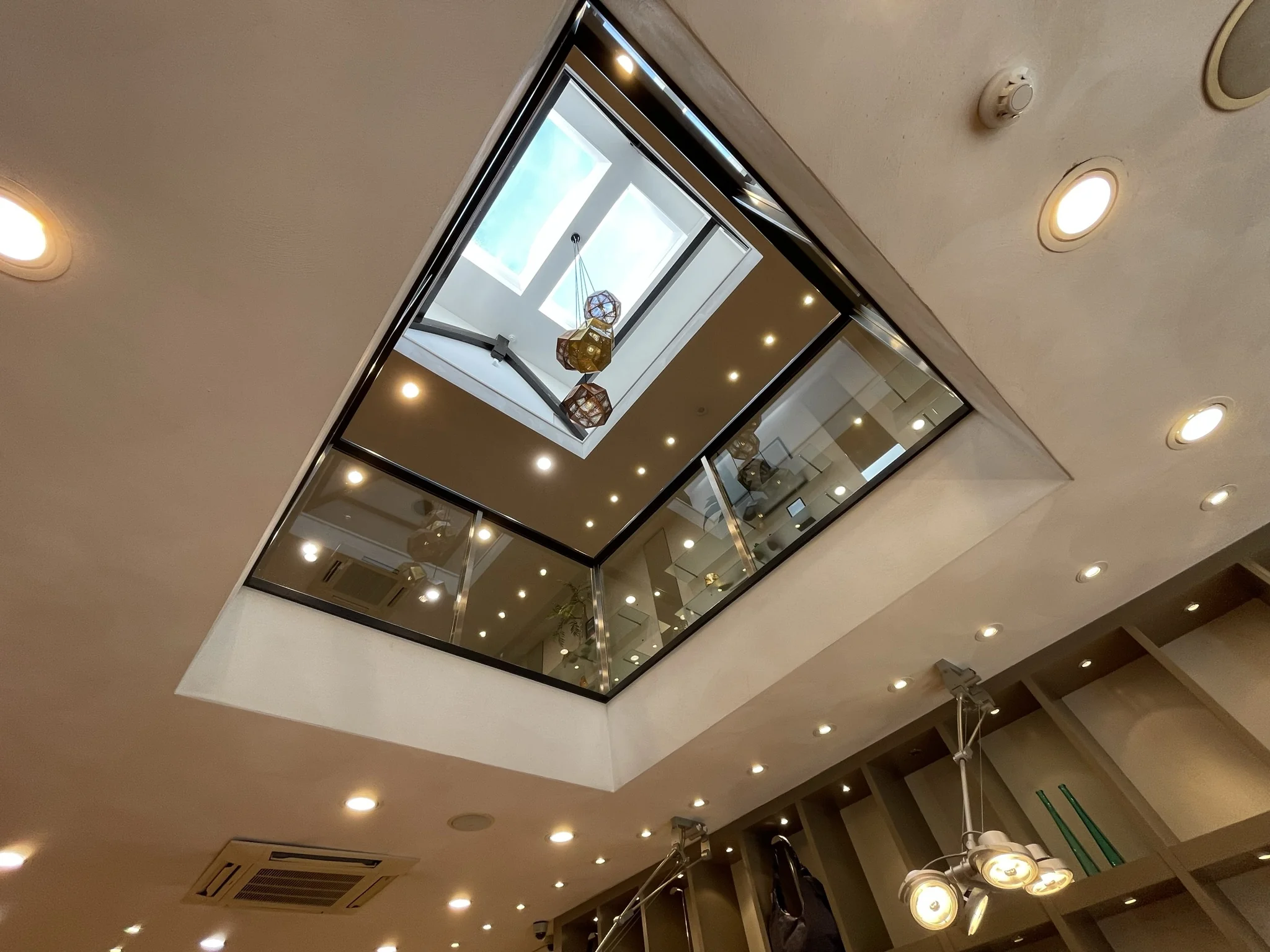 Doorkijk naar een glazen vide met hanglampen en dakraam in een modern interieur aan de Molendijk.