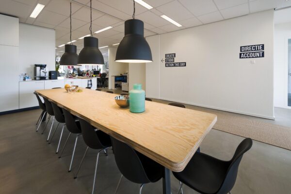Moderne kantoorruimte aan de Helicopterstraat met een lange houten vergadertafel, zwarte stoelen en grote hanglampen.
