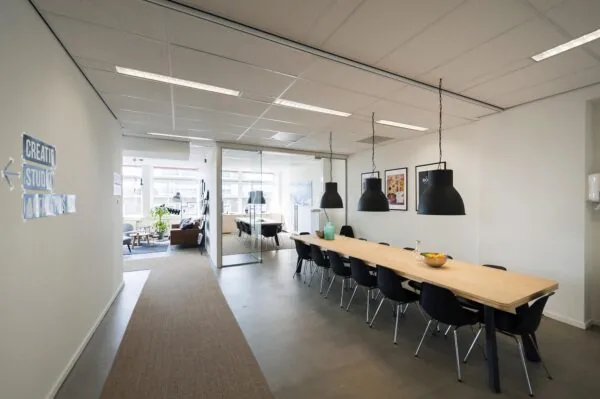 Moderne kantoorruimte aan de Helicopterstraat met een lange vergadertafel, hanglampen en een glazen vergaderruimte.