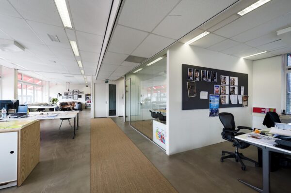 Modern kantoorinterieur aan de Helicopterstraat met glazen vergaderruimte, bureaus en een prikbord met posters en foto's.