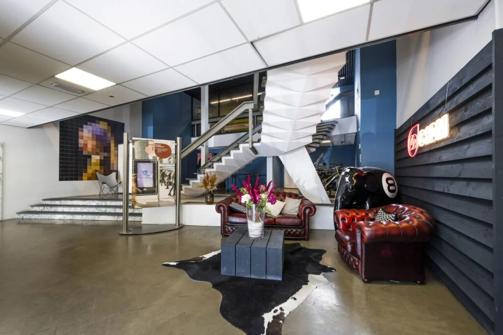 Sfeervolle lobby aan de Vliegtuigstraat met leren fauteuils, kunst aan de muur en een witte designtrap.