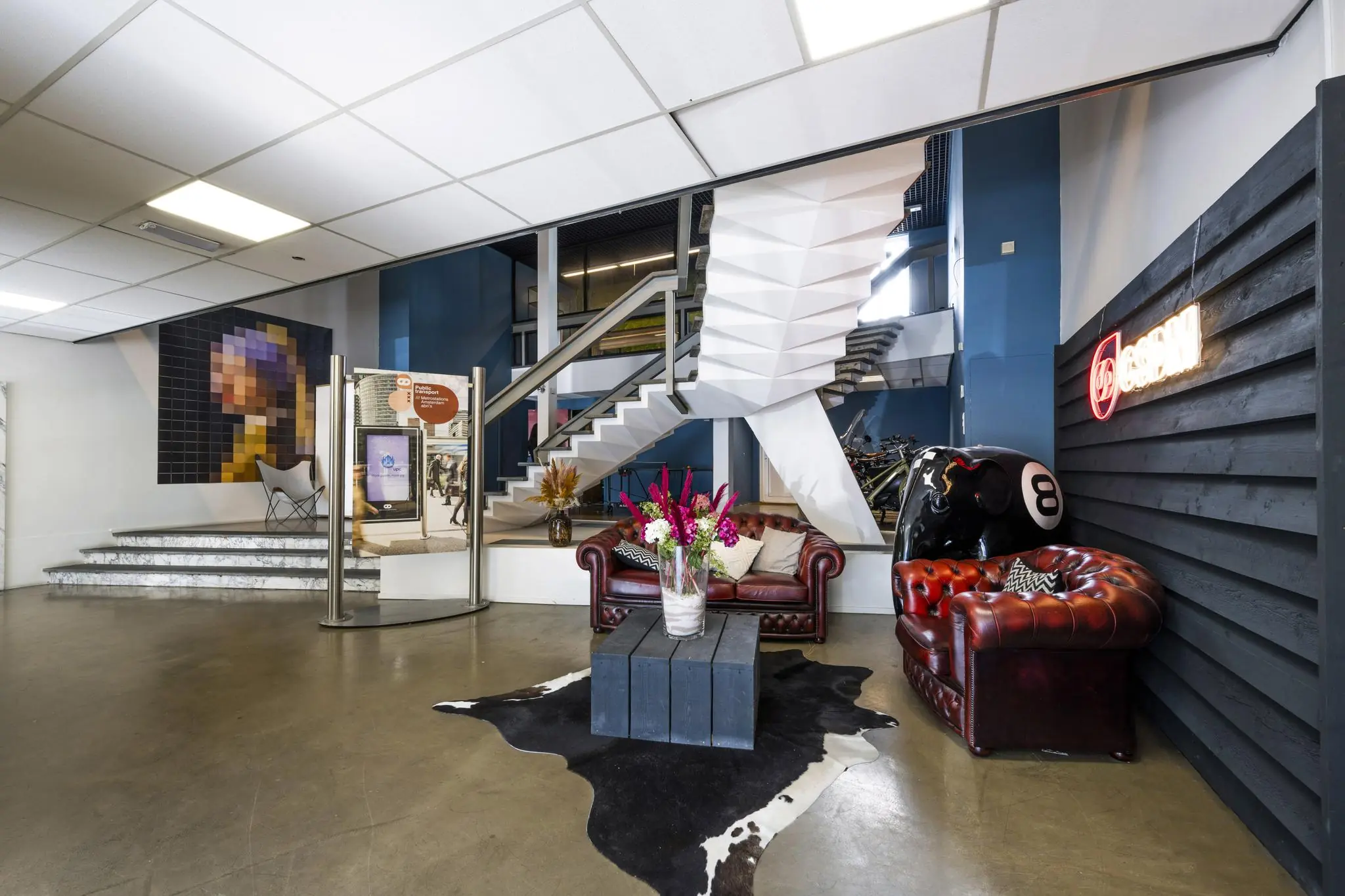 Sfeervolle lobby aan de Vliegtuigstraat met leren fauteuils, kunst aan de muur en een witte designtrap.