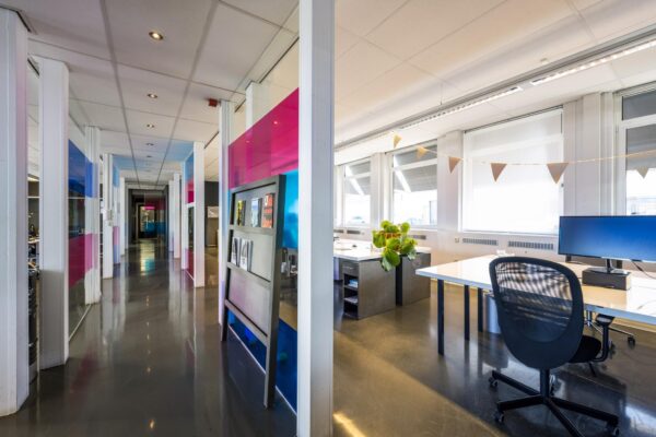 Modern kantoorinterieur aan de Vliegtuigstraat met kleurrijke glazen wanden, bureaus en veel daglicht.