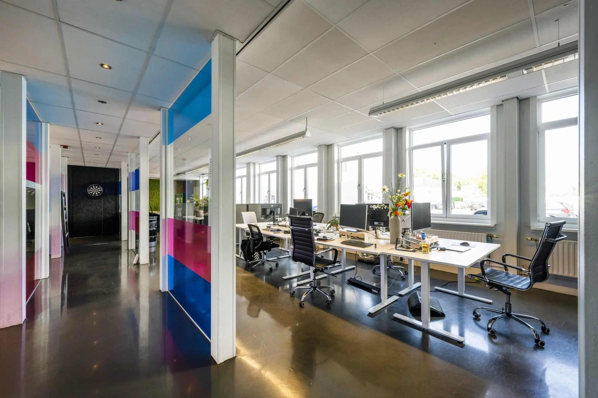 Modern kantoorinterieur aan de Vliegtuigstraat met open werkplekken, grote ramen en kleurrijke glazen scheidingspanelen.