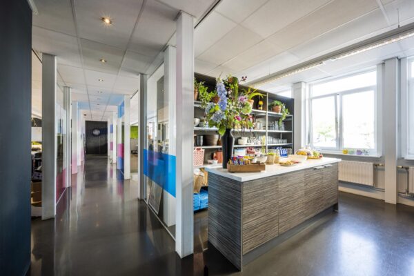 Moderne kantoorruimte aan de Vliegtuigstraat met een open keuken voorzien van bloemen, snacks en daglicht.