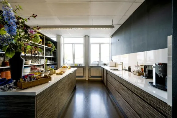 Moderne bedrijfskeuken aan de Vliegtuigstraat met houten kasten, wit aanrechtblad en open rekken met etenswaren en planten.