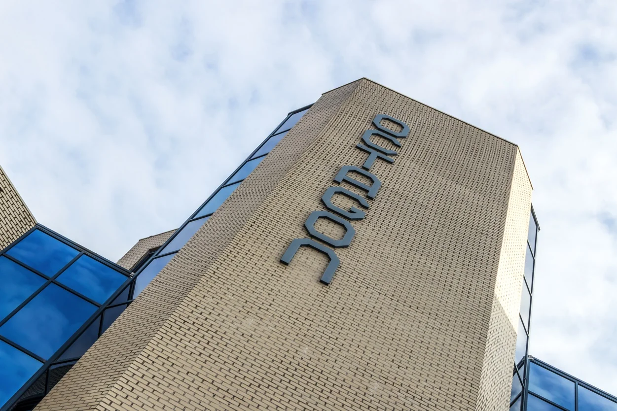 Hoekige gevel van een modern kantoorgebouw aan de Dukatenburg, met spiegelende ramen en verticale belettering.