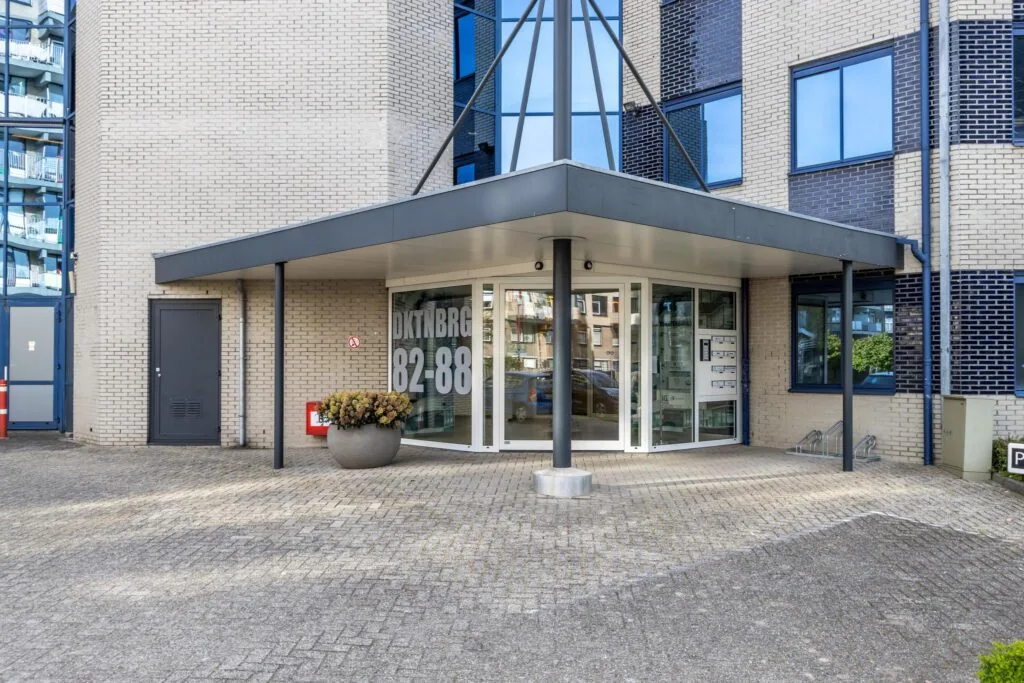 Ingang van een modern appartementencomplex aan de Dukatenburg 82-88 met overkapping en glazen voordeur.