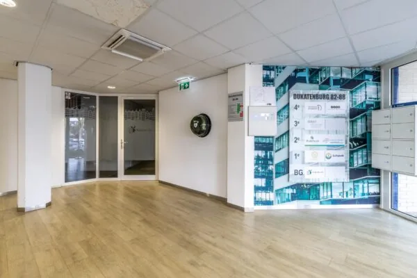 Ingang en hal van het bedrijfsverzamelgebouw Dukatenburg 82-88 met bedrijvenbord en AED aan de muur.