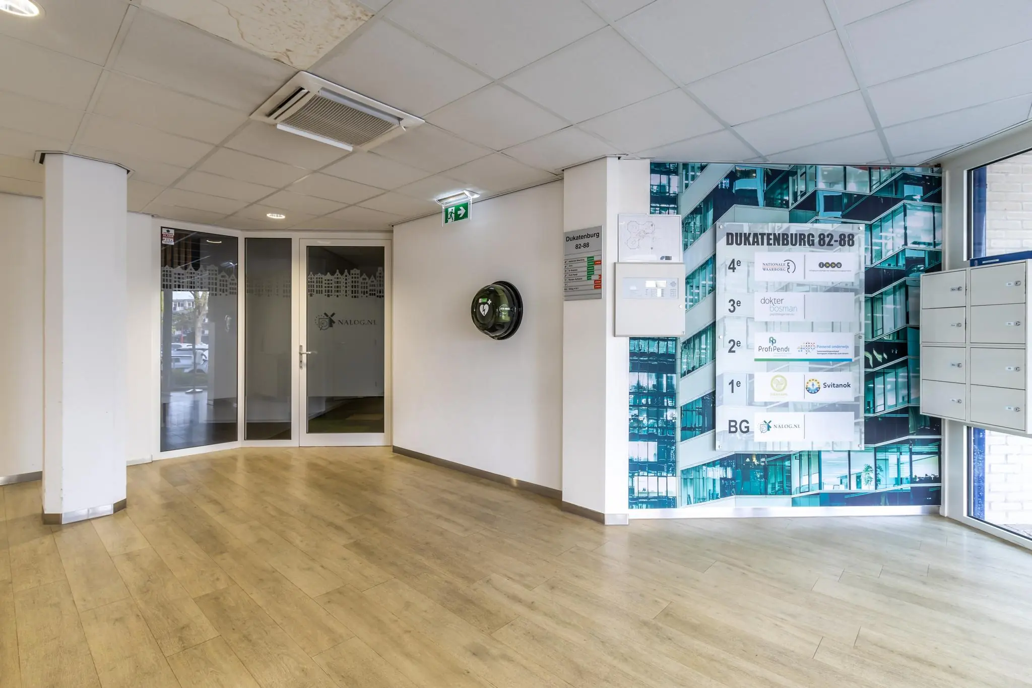 Ingang en hal van het bedrijfsverzamelgebouw Dukatenburg 82-88 met bedrijvenbord en AED aan de muur.