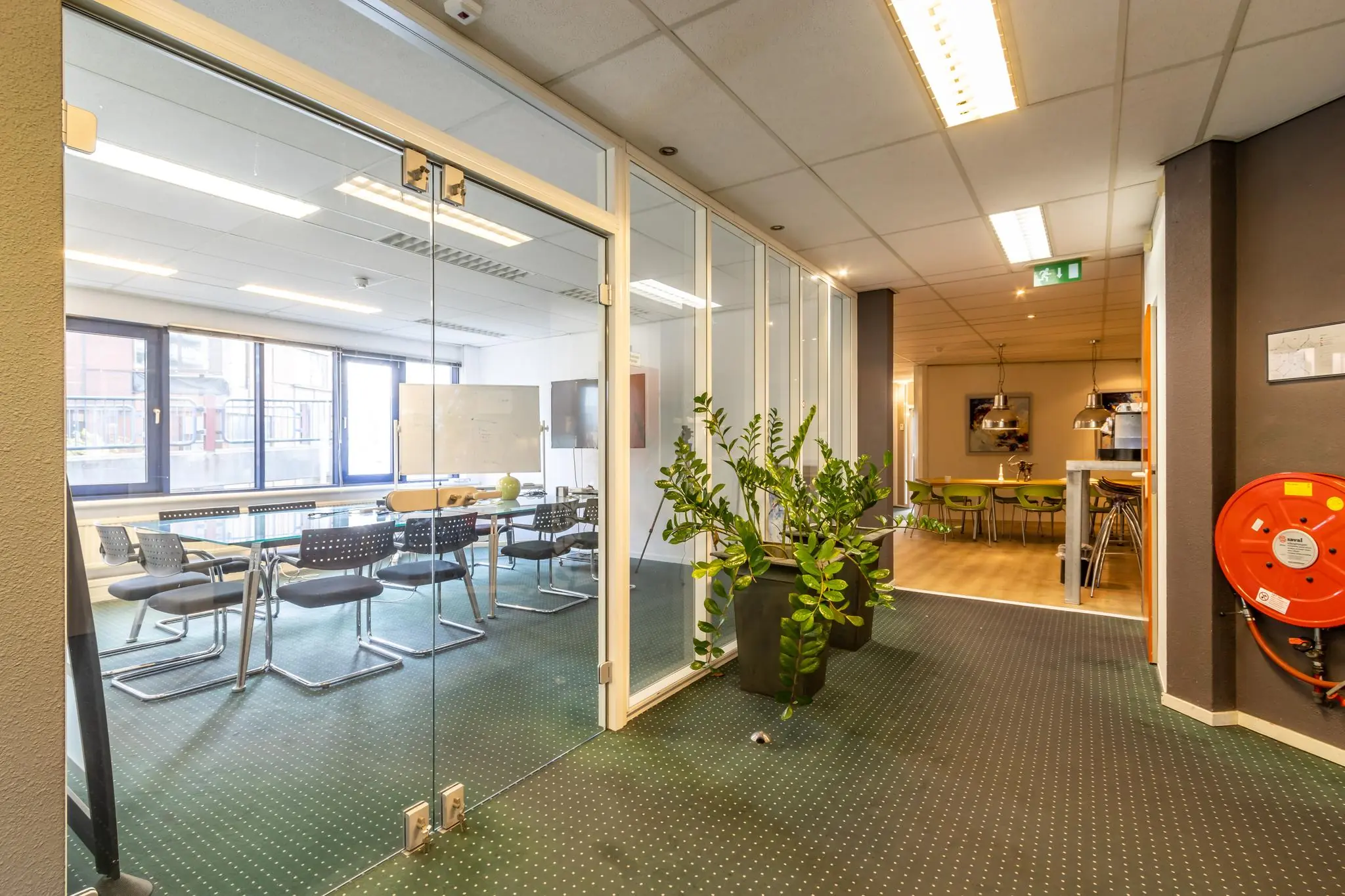 Moderne kantoorruimte in Dukatenburg met vergaderruimte, glazen wanden, planten en een aangrenzende kantine.