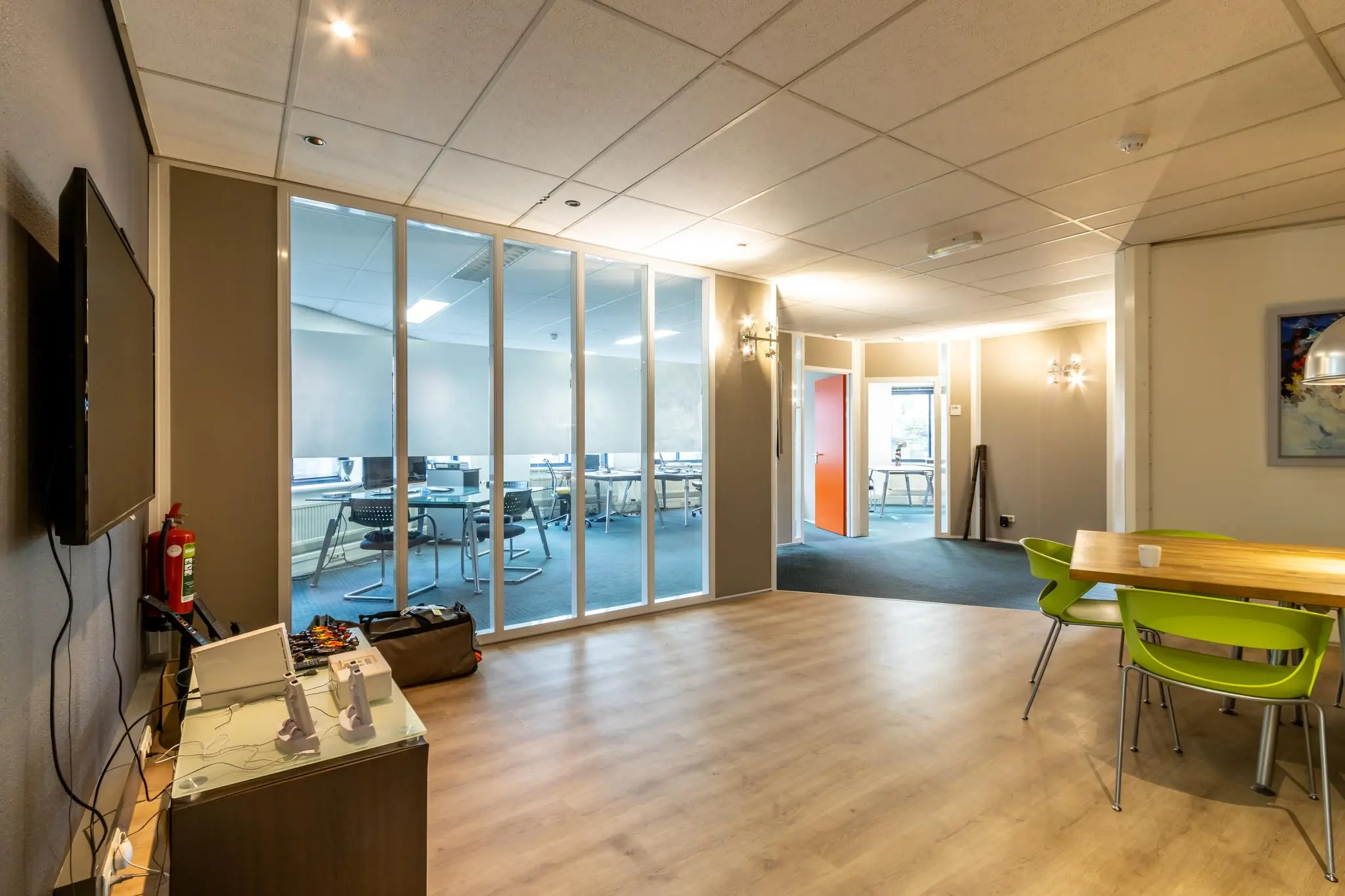 Moderne kantoorruimte aan de Dukatenburg met glazen vergaderruimte, houten vloer en felgroene stoelen rond een tafel.