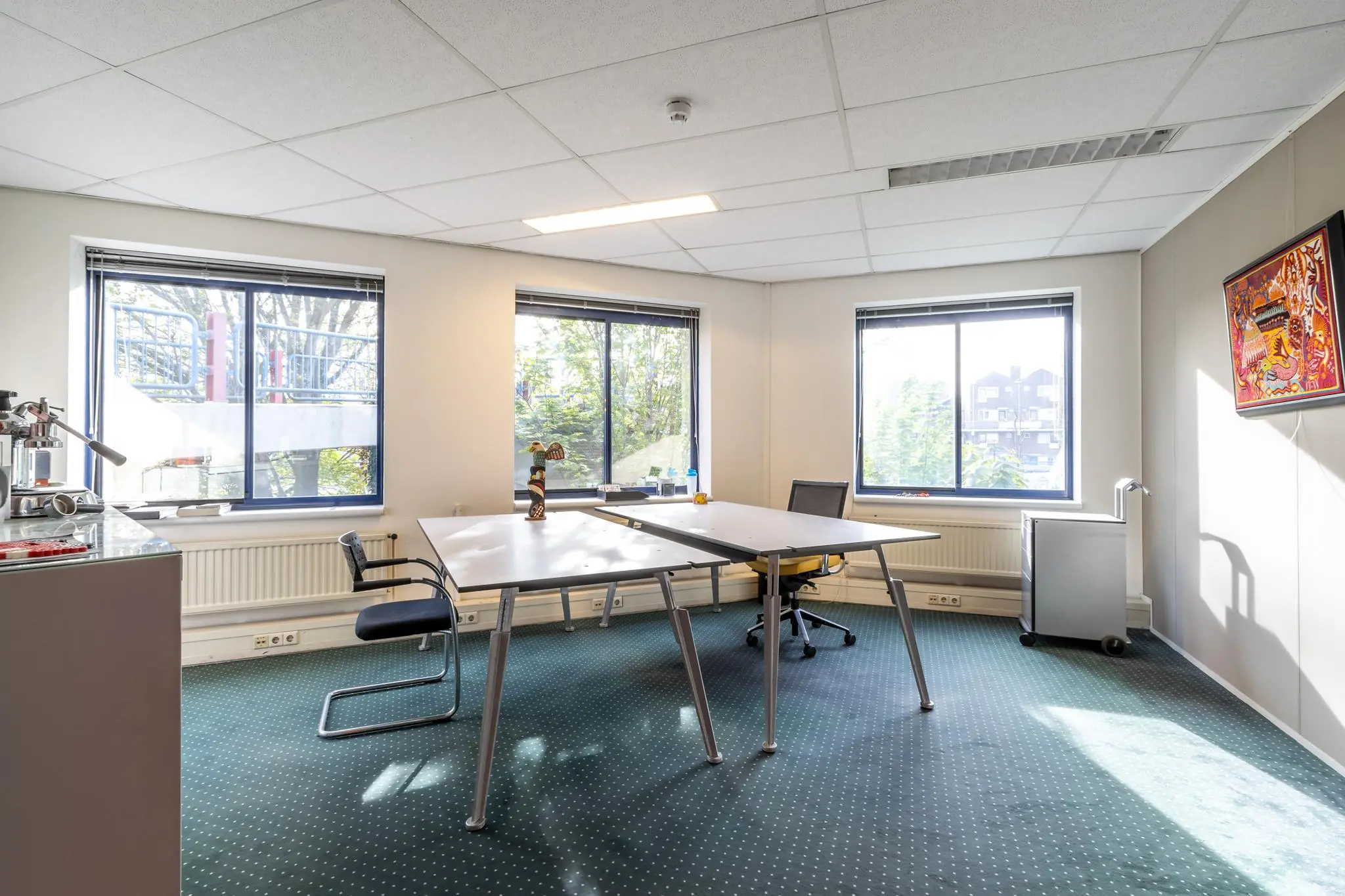 Licht en modern kantoor met drie ramen, twee bureaus, bureaustoelen en een kunstwerk aan de muur in gebouw Dukatenburg.