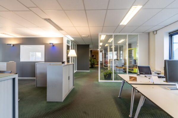 Modern kantoorpand aan de Dukatenburg met glazen wanden, bureaus en groene vloerbedekking.