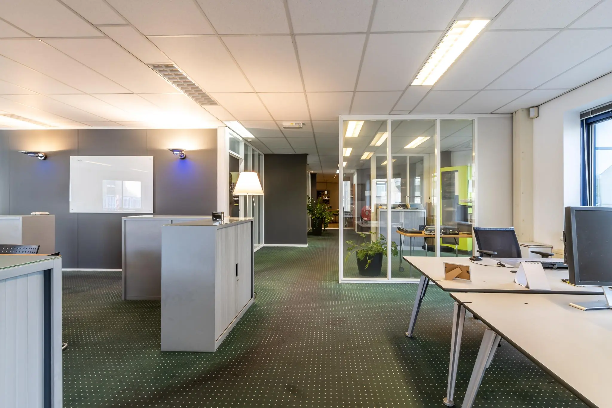 Modern kantoorpand aan de Dukatenburg met glazen wanden, bureaus en groene vloerbedekking.