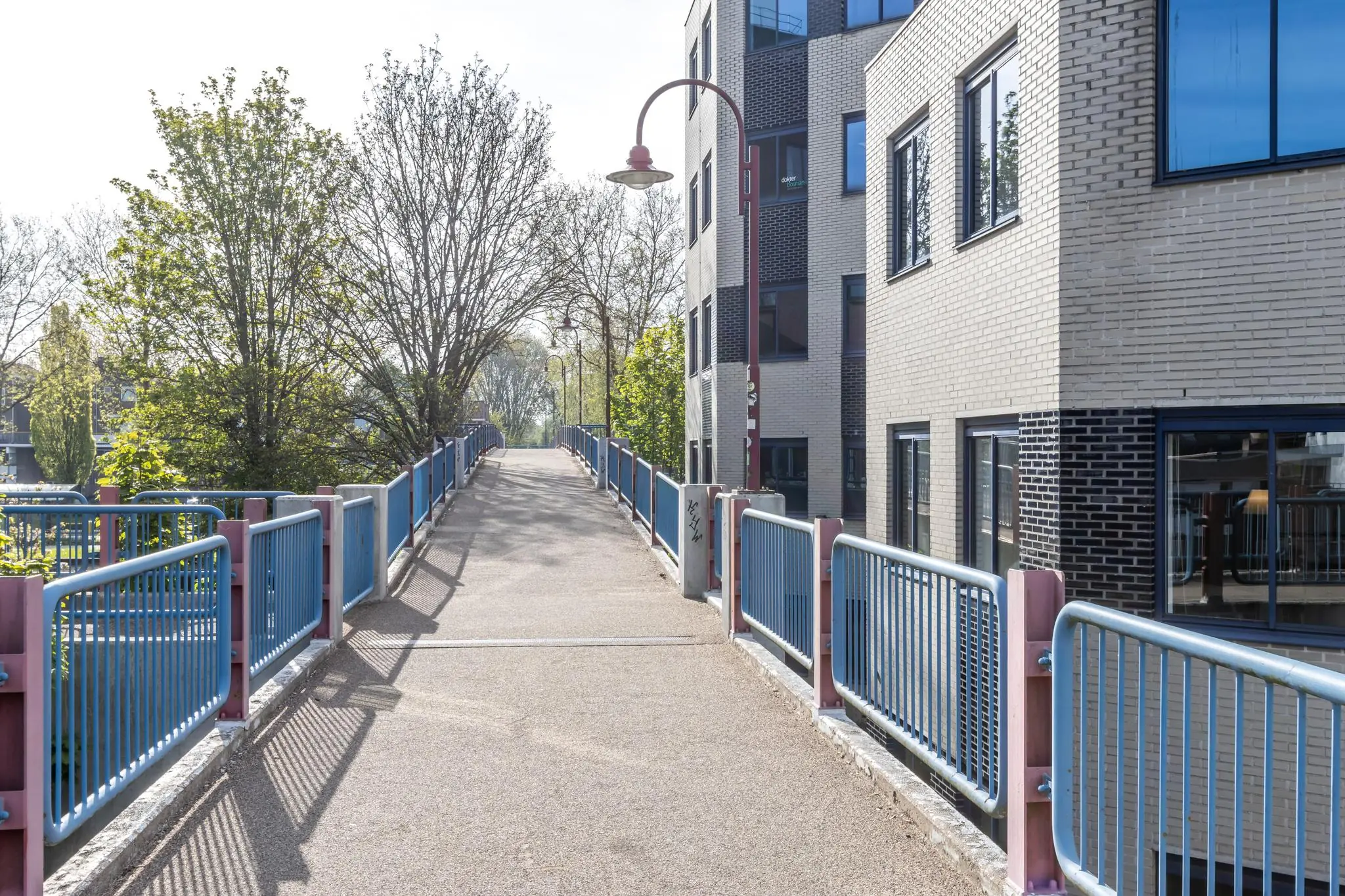 Voetgangersbrug met blauw-roze hekwerk naast een modern gebouw aan de Dukatenburg.