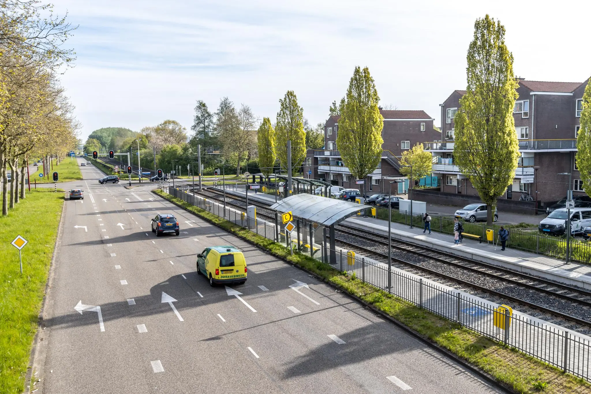 Straatbeeld van halte Dukatenburg in Nieuwegein met een drukke weg, trambaan en enkele wachtende reizigers.