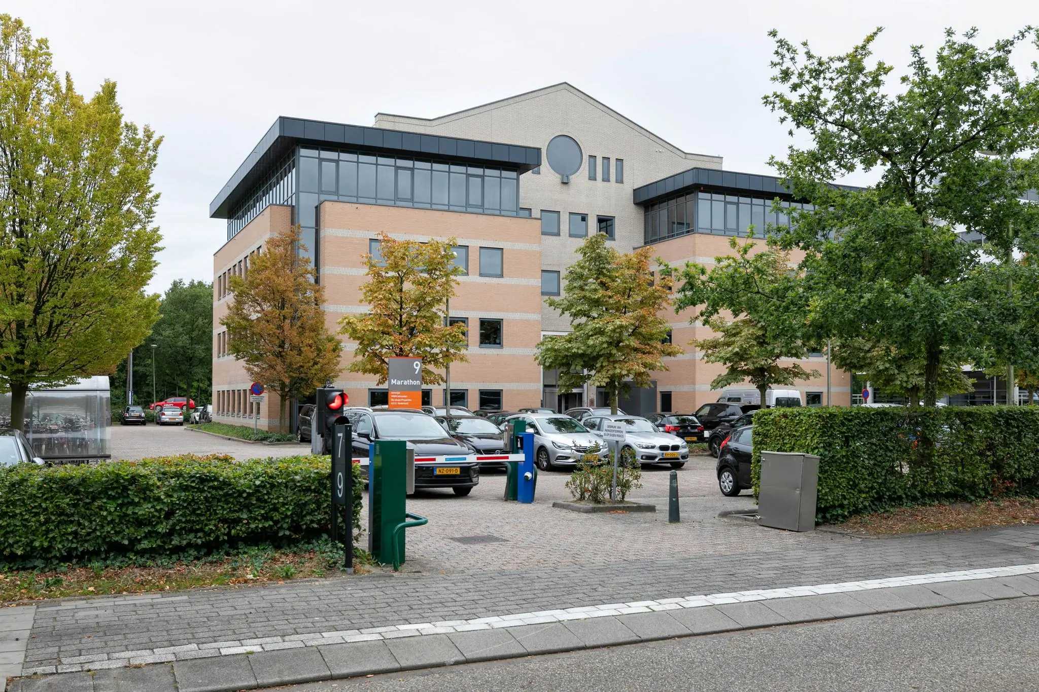 Kantoorgebouw Marathon 9 met parkeerterrein en omringende bomen in herfstkleuren.