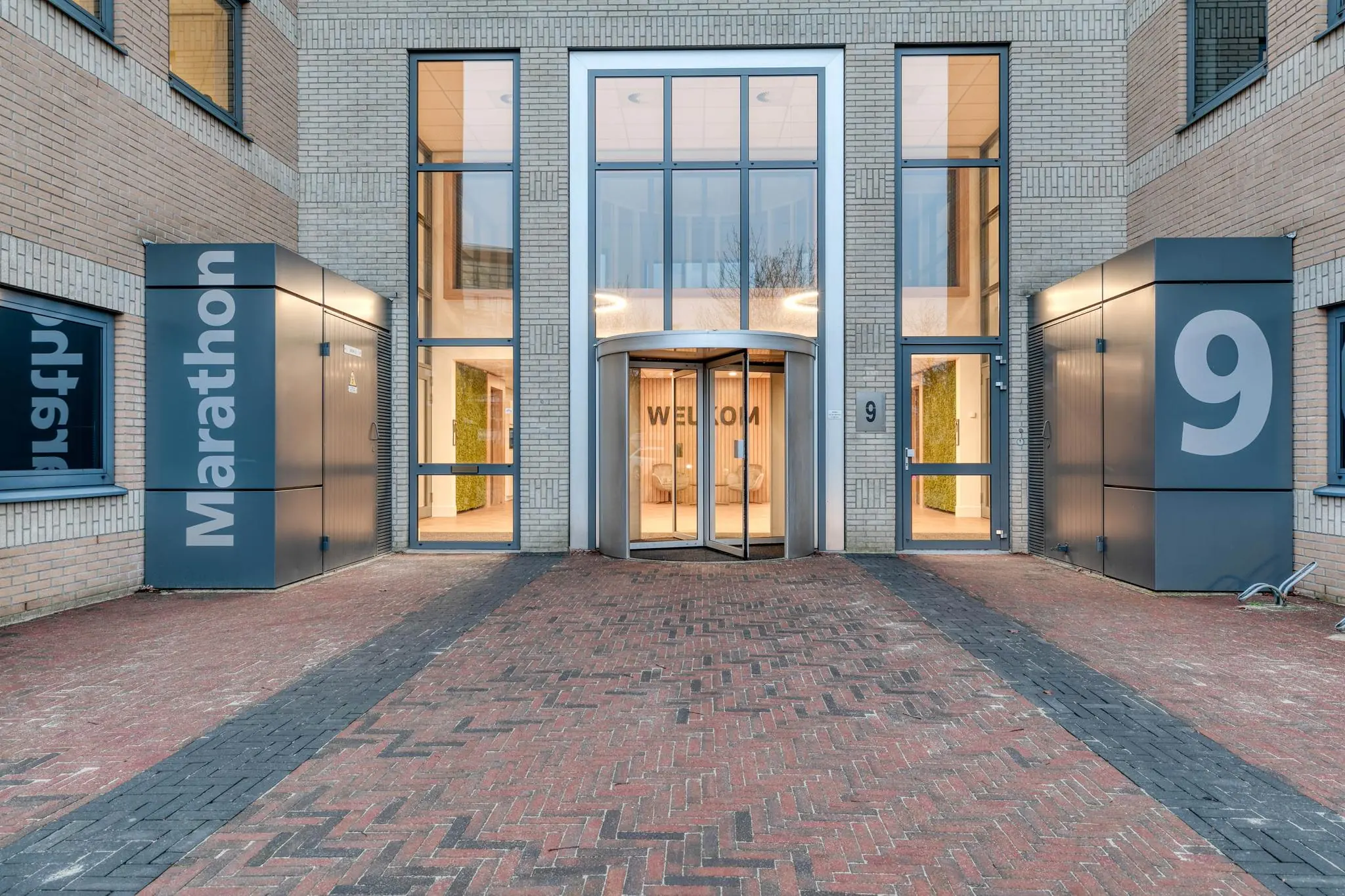 Ingang van kantoorgebouw Marathon 9 met automatische draaideur en moderne gevel.