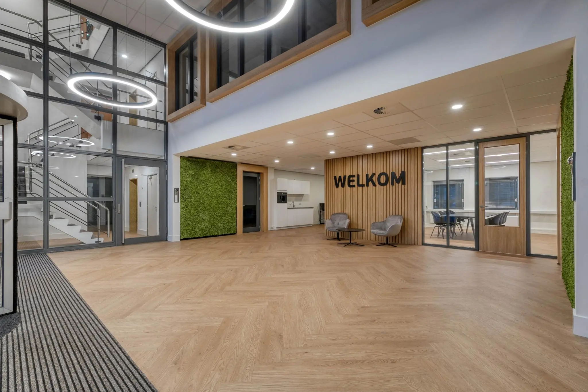 Moderne kantoorentree met houten vloer, groene wandaccenten en een 'WELKOM'-bord bij een wachtruimte.