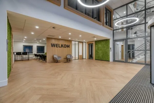 Moderne en ruime entreehal met houten vloer, groene accenten en de tekst "WELKOM" op de muur.
