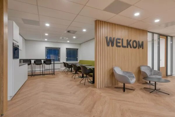 Moderne kantoorruimte met een zithoek, hoge stoelen en een houten wand met het woord "WELKOM".