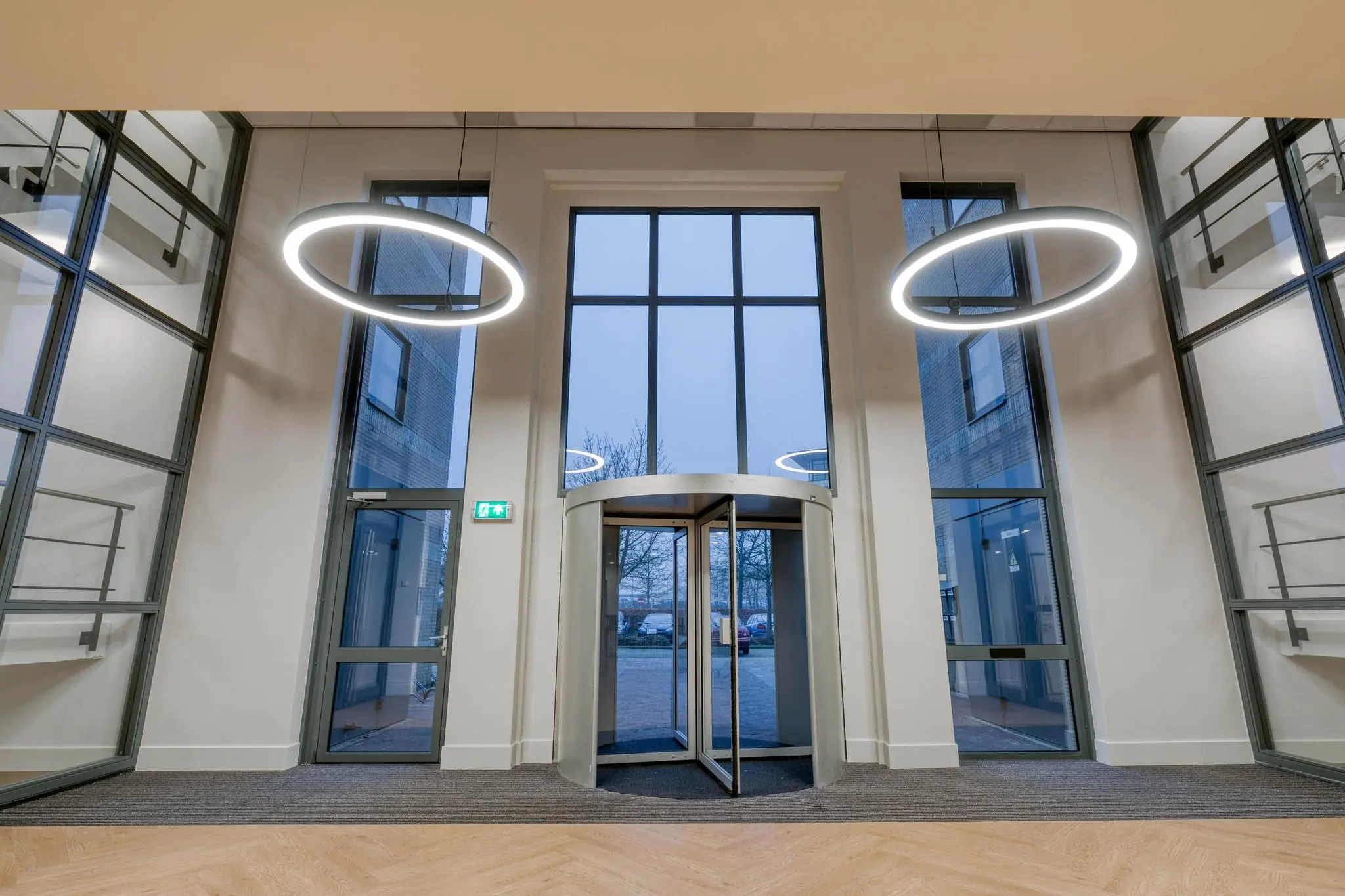 Moderne entreehal met een glazen draaideur, hoge ramen en ronde hanglampen.
