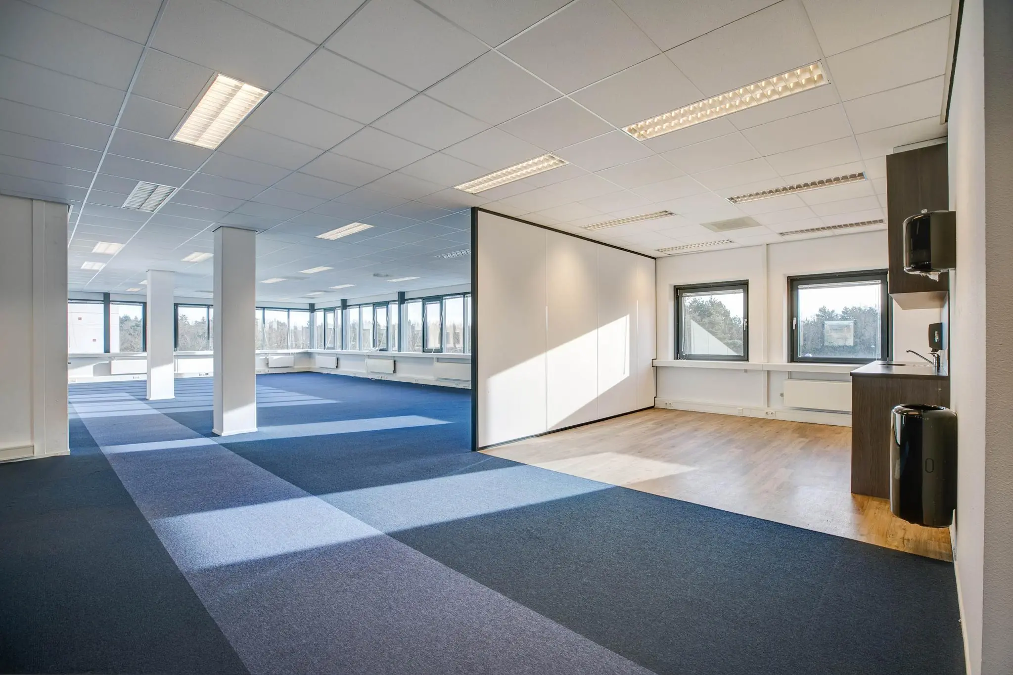 Licht en ruim kantoorpand met open werkruimte, grote ramen en een aparte kitchenette.