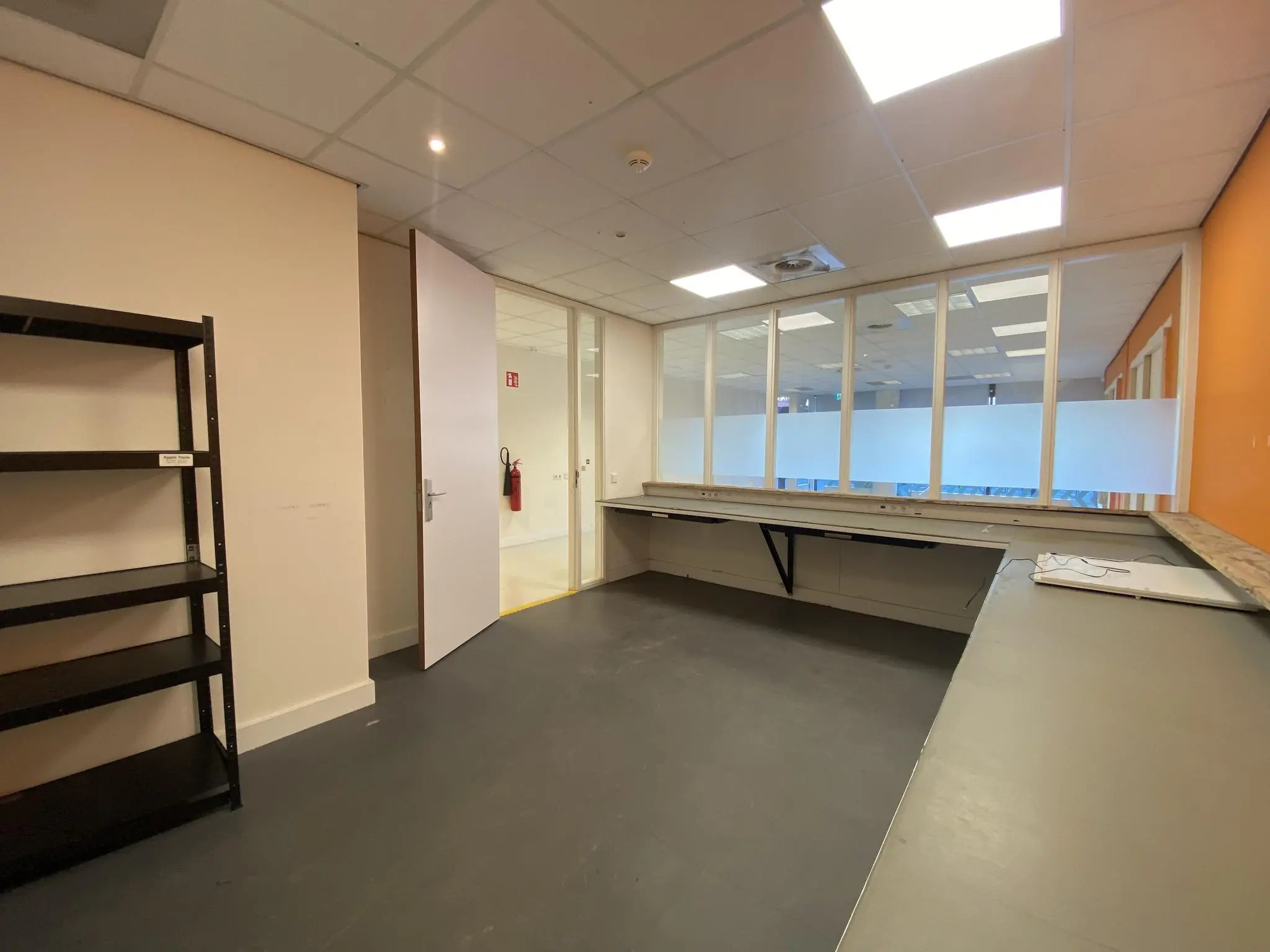 Lege kantoorruimte aan het Herculesplein met werkbladen langs de muur en een open deur naar de gang.