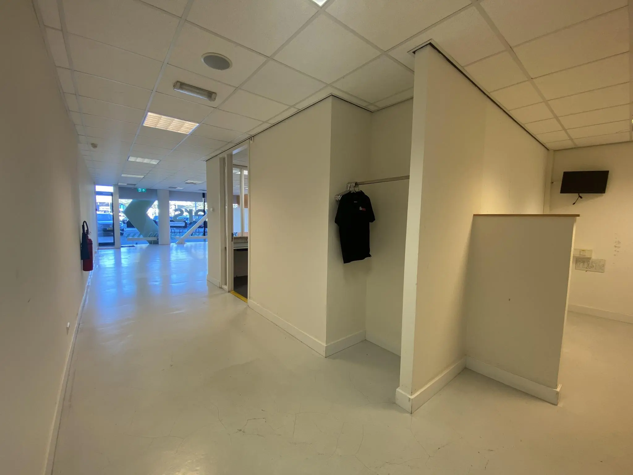 Witgeschilderde gang in een kantoorpand aan het Herculesplein met een open ruimte, een zwarte shirt aan een rek en zicht op de glazen entree.