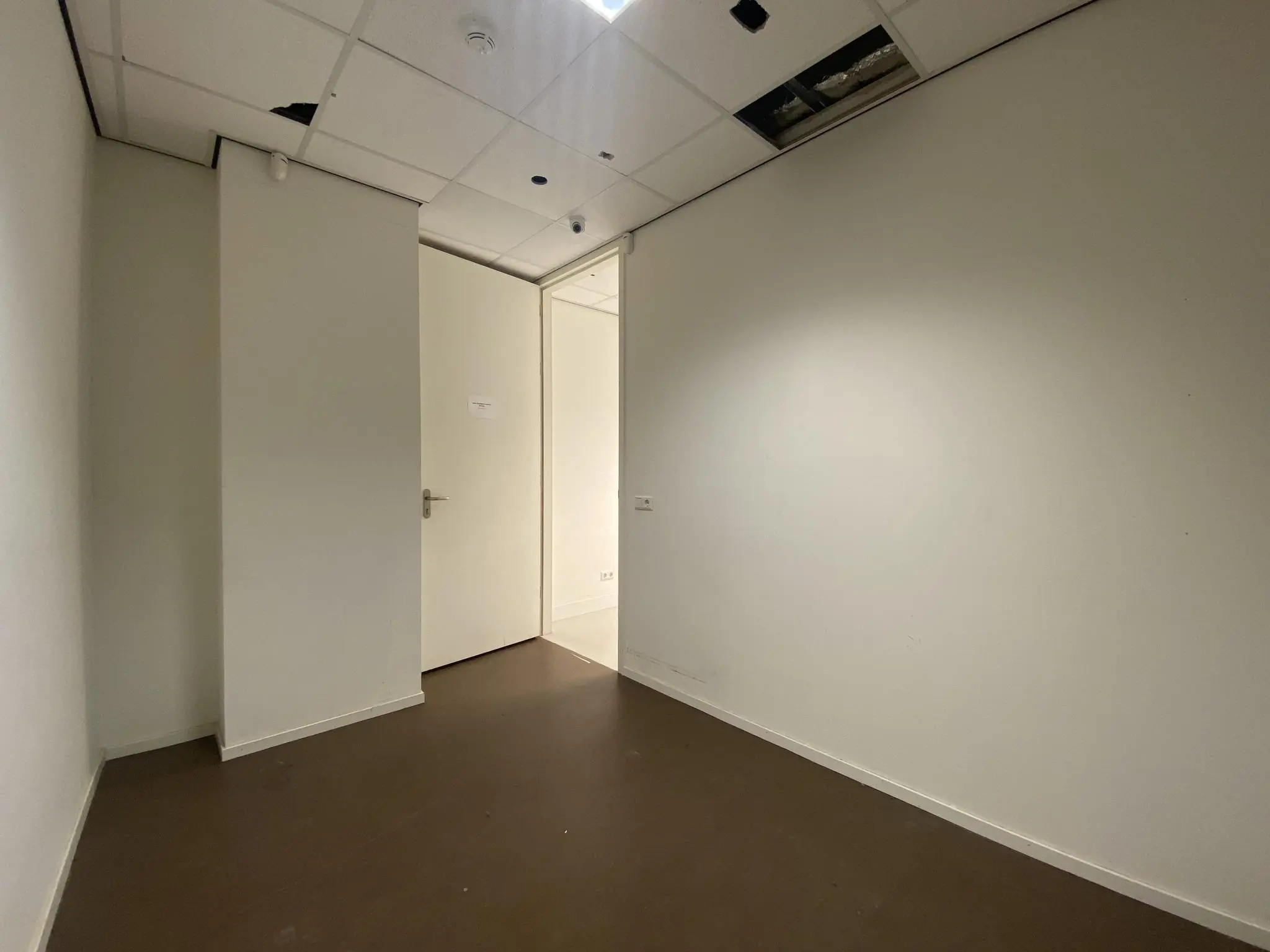 Lege, witte kamer op Herculesplein met een deels open systeemplafond en een gesloten deur.