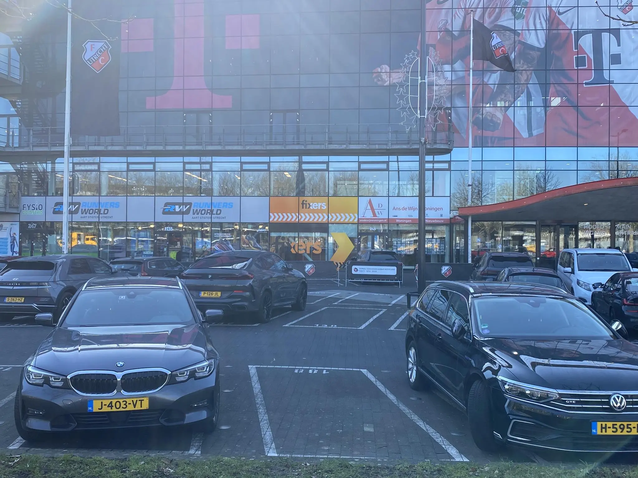 Parkeerterrein voor Stadion Galgenwaard aan het Herculesplein met auto's en gevelreclame van FC Utrecht en T-Mobile.